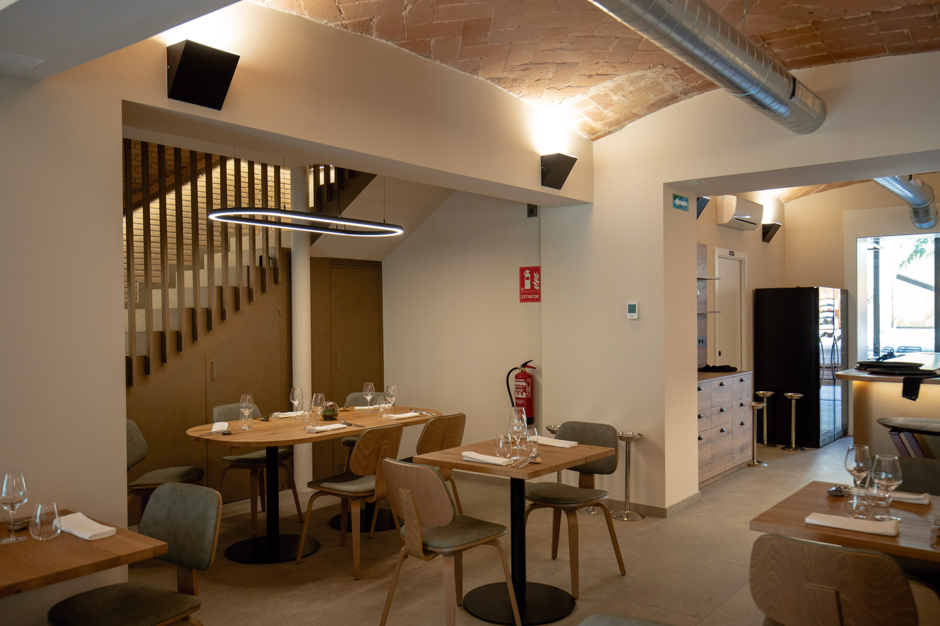 Aplique de pared en color negro ilumina la sala principal de un restaurante junto con una luminaria circular Tundra que ilumina una mesa rectangular