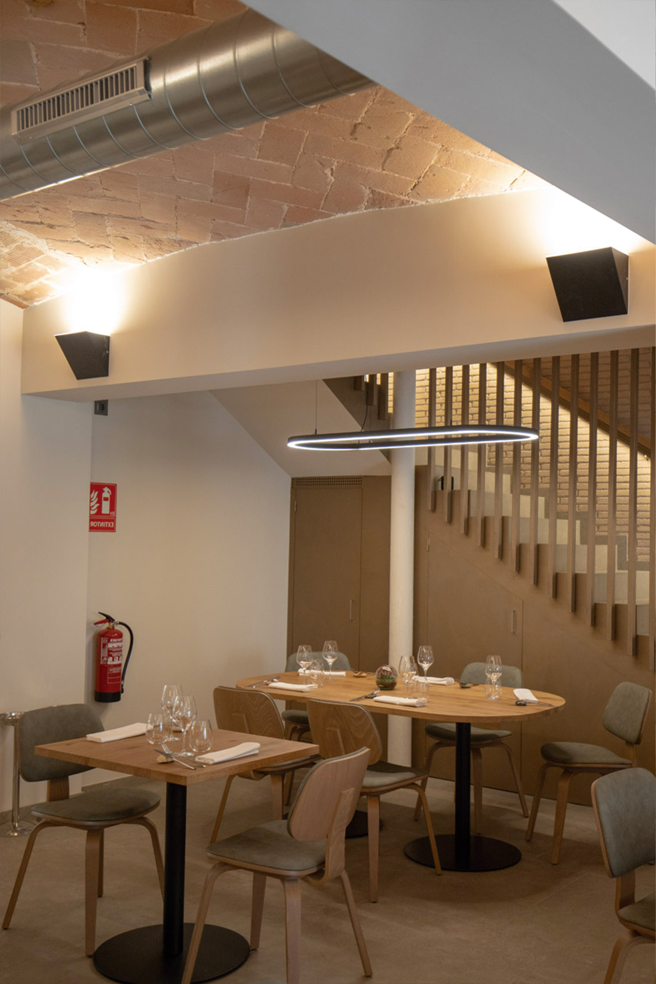 Aplique de pared en color negro ilumina la sala principal de un restaurante junto con una luminaria circular Tundra que ilumina una mesa rectangular